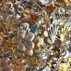 May include: A collection of assorted metallic sequins in gold and silver tones. The shapes include flowers, stars, crescent moons, butterflies, and geometric fan patterns. Each piece features a reflective, shiny finish with small holes for sewing.