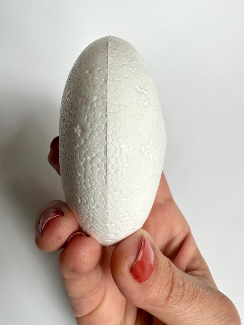 May include: A white styrofoam egg-shaped craft supply. The egg is smooth and has a textured surface.