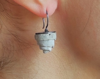 May include: A pair of silver earrings with a concrete spiral design. The earrings are hanging from a person's ear.