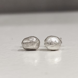 Puede incluir: Un par de pendientes de botón de plata con un diseño texturizado en forma de guijarro.