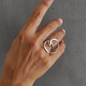 Może przedstawiać: Srebrny pierścionek z sercowatym wzorem. Pierścionek składa się z dwóch splecionych ze sobą kół.