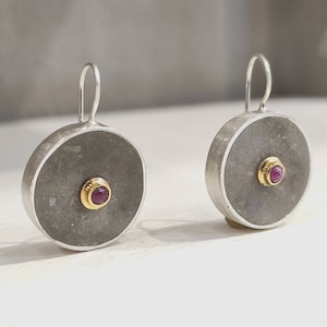 Peut inclure: Une paire de boucles d'oreilles en argent avec une surface ronde, grise et texturée et une petite pierre précieuse rose sertie dans une bélière en or.
