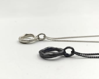 Puede incluir: Dos collares de plata con un colgante único de forma orgánica. Un colgante es plateado y el otro es negro.