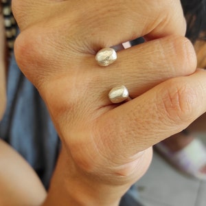 Puede incluir: Dos anillos de plata con un diseño redondeado y texturado. Los anillos se llevan en el dedo medio de una mano.