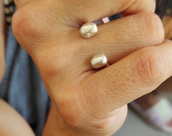May include: Two silver rings with a rounded, textured design. The rings are worn on the middle finger of a hand.