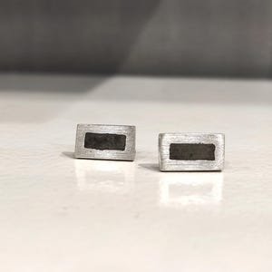 May include: A pair of silver earrings with a rectangular shape and a black inlay.