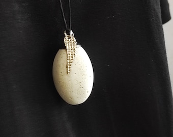 May include: A white oval pendant with a gold chain and a gold beaded detail hanging from a black cord necklace.