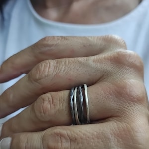 Può includere: Un anello d'argento con più bande, ognuna con una texture e una finitura leggermente diverse. Le bande sono impilate l'una sull'altra, creando un look unico e moderno.