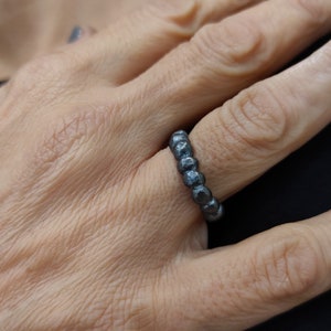 Könnte beinhalten: Ein silberner Ring mit einem Perlenmuster. Der Ring wird an einem Finger getragen.