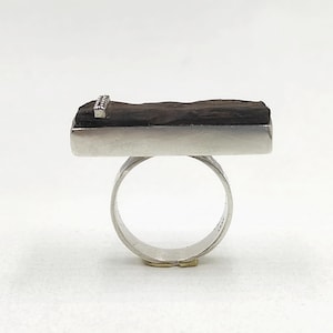 May include: A silver ring with a rectangular black stone set on top. The stone has a silver band across the top with small silver accents.