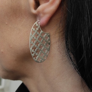 Puede incluir: Pendientes de aro de plata con un diseño recortado que presenta un patrón repetitivo de pequeñas flores.
