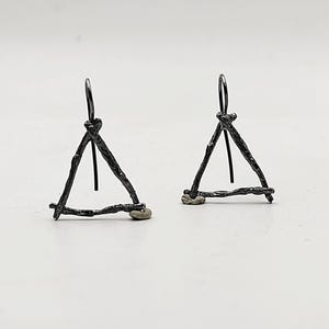 Può includere: Un paio di orecchini triangolari in argento con un delicato design a filo. Gli orecchini sono realizzati in filo ritorto e hanno uno stile semplice e minimalista.