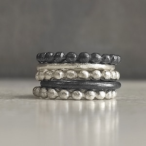 Peut inclure: Un ensemble de cinq bagues en argent et noir à perles empilées les unes sur les autres. Les bagues ont toutes la même largeur et un design simple et élégant.