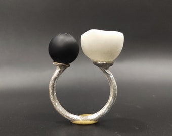 May include: A silver ring with a black and white orb on each side. The ring is made of metal and has a smooth finish.
