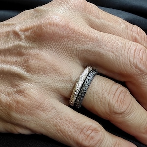 Könnte beinhalten: Zwei silberne Ringe mit einer strukturierten Oberfläche. Der obere Ring ist schwarz und der untere Ring ist silber.