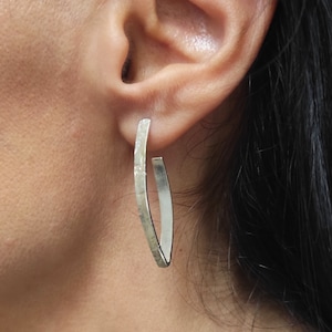 Peut inclure: Boucles d'oreilles créoles en argent avec une texture martelée. Les boucles d'oreilles sont de forme ovale et ont un design légèrement incurvé.