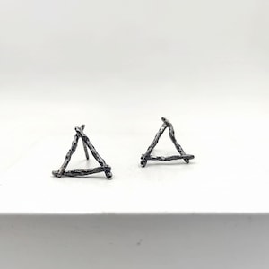 May include: A pair of silver triangle earrings made of thin, textured metal. The earrings are simple and modern in design.
