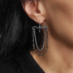 May include: A pair of dangle earrings with a black chain and brown gemstone beads. The earrings feature a black metal design at the top.