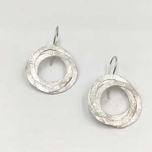 Peut inclure: Une paire de boucles d'oreilles pendantes en argent avec un design circulaire texturé. Chaque boucle d'oreille présente trois cercles qui se chevauchent.