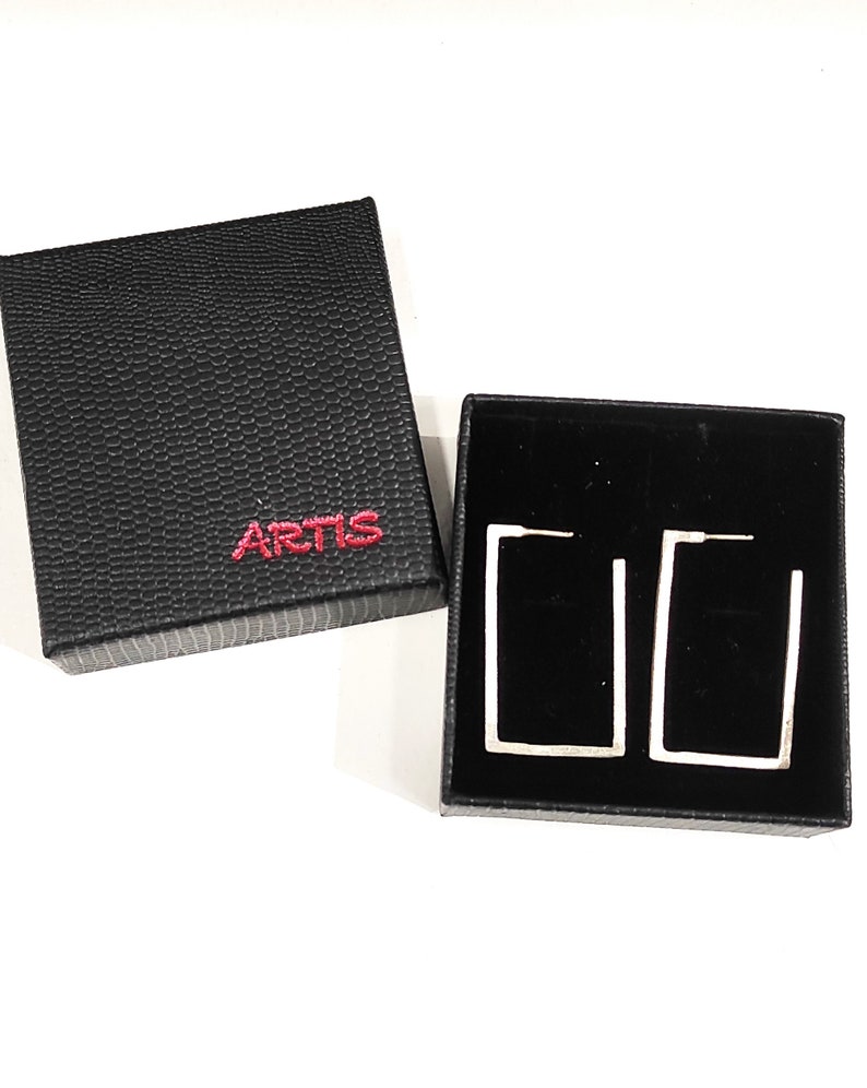 May include: A pair of silver rectangular hoop earrings in a black box with the word "ARTIS" printed on the top.