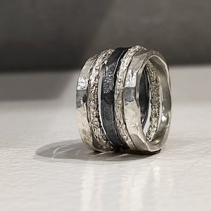 Op de afbeelding: Een set van vier zilveren en zwarte ringen met een textuur. De ringen zijn op elkaar gestapeld.