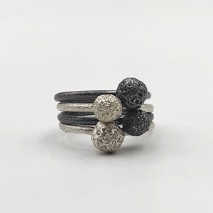 Puede incluir: Un anillo de plata con tres esferas texturizadas, dos negras y una plateada.