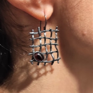 May include: A pair of silver earrings with a geometric design and a dark red gemstone in the centre.