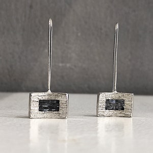 May include: A pair of silver earrings with a square design. Each earring has a small black square in the centre.