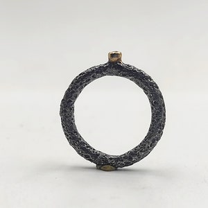 May include: A black ring with a textured surface and a small gold accent on top.