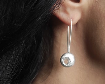 May include: Silver dangle earrings with a textured round disc pendant. The disc has a small hole in the centre.