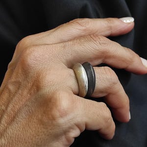 May include: A silver and black ring with a unique design. The ring is worn on the index finger of a hand.