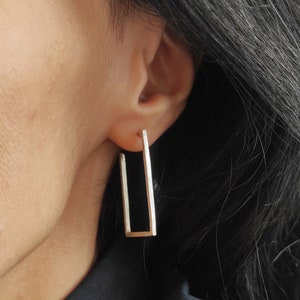 May include: Silver rectangle hoop earrings with a textured finish.