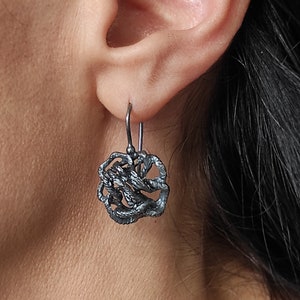 Puede incluir: Un par de pendientes de plata con un diseño único e intrincado. Los pendientes están hechos de metal retorcido y anudado que crea un efecto tridimensional.