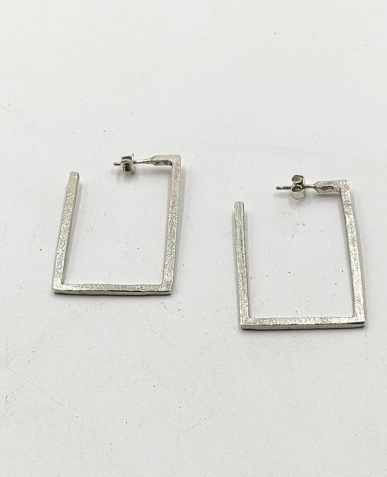 May include: A pair of silver square hoop earrings with a textured finish.