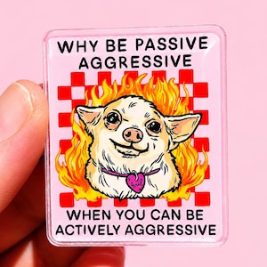 Op de afbeelding: Een rechthoekige acryl pin met een lichtroze achtergrond en een rood dambordpatroon. In het midden is een beige hond omringd door gele en oranje vlammen. De tekst luidt: WHY BE PASSIVE AGGRESSIVE WHEN YOU CAN BE ACTIVELY AGGRESSIVE.
