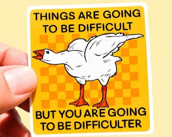 May include: A square sticker with a yellow background featuring a white goose with orange feet and beak. The text reads: THINGS ARE GOING TO BE DIFFICULT BUT YOU ARE GOING TO BE DIFFICULTER. The background has a subtle orange checkered pattern.