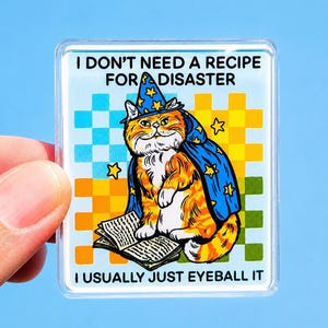 Op de afbeelding: Een vierkante acrylaatmagneet met een oranje cyperse kat die een blauwe tovenaarsmuts en cape met gele sterren draagt. De kat zit bij een open boek. De tekst luidt I DON'T NEED A RECIPE FOR DISASTER en I USUALLY JUST EYEBALL IT op een geblokte achtergrond.