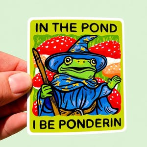 May include: A rectangular sticker featuring a green frog wearing a blue wizard hat and robe with yellow stars, holding a wooden staff. The background shows red mushrooms with white spots. The text reads IN THE POND I BE PONDERIN.