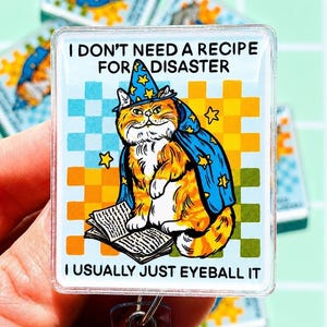 May include: A rectangular acrylic badge reel featuring an orange tabby cat wearing a blue wizard hat and cape with yellow stars. The cat sits by an open book against a checkered background. Text reads: I DON'T NEED A RECIPE FOR DISASTER I USUALLY JUST EYEBALL IT.