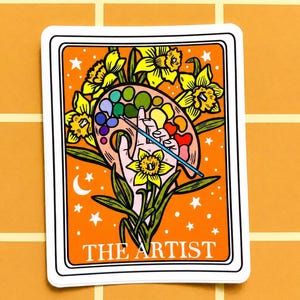 May include: A sticker featuring a colorful illustration of a hand holding a paint palette with a paintbrush, surrounded by yellow daffodils. The text "THE ARTIST" is at the bottom, set against an orange background.
