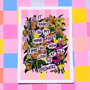 May include: A colorful art print featuring a bouquet of flowers and butterflies. The print includes the text "It rained in my mind for a time but now look at all the flowers." The artwork is set against a pink and yellow background.