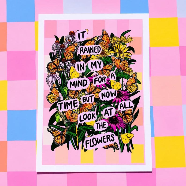 May include: A colorful art print featuring a bouquet of flowers and butterflies. The print includes the text "It rained in my mind for a time but now look at all the flowers." The artwork is set against a pink and yellow background.