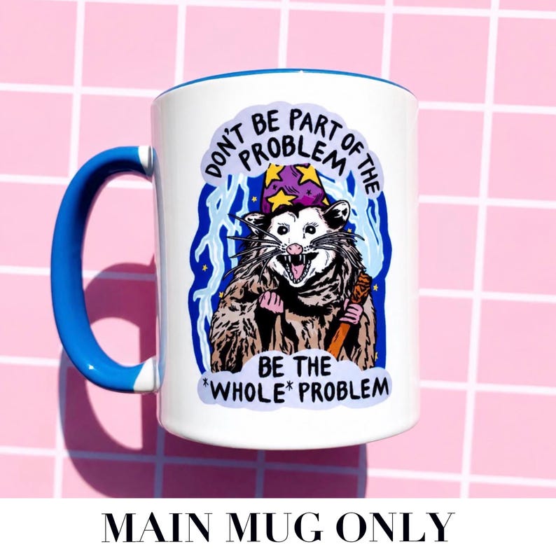 Pu&ograve; includere: Tazza in ceramica bianca con manico e bordo blu. La tazza presenta un opossum dei cartoni animati con un cappello da mago e un bastone, con il testo "DON'T BE PART OF THE PROBLEM BE THE *WHOLE* PROBLEM."