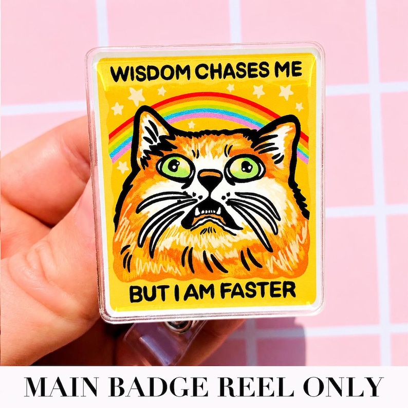 May include: A rectangular badge reel featuring a yellow background with a graphic of an orange cat with wide green eyes. Above the cat is a rainbow and white stars. The text reads WISDOM CHASES ME BUT I AM FASTER in black capital letters.