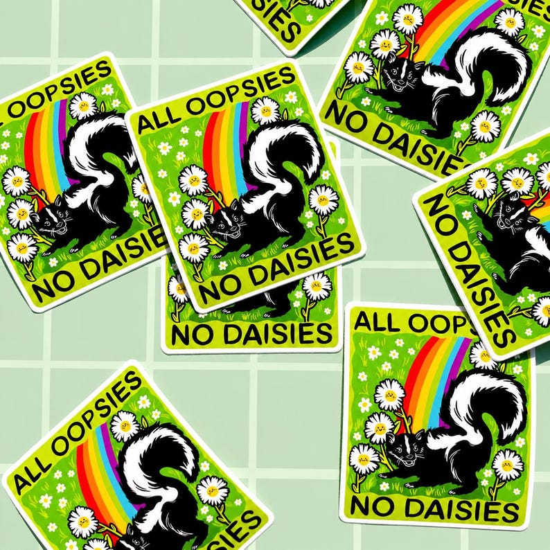 May include: A rectangular sticker featuring a black and white skunk standing in a green field with white daisies and a rainbow. The text ALL OOPSIES NO DAISIES is printed in black capital letters at the top and bottom of the sticker design.