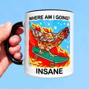 Puede incluir: Una taza de cer&aacute;mica blanca con asa y borde negros, que presenta un gr&aacute;fico de un pollo marr&oacute;n con gafas de sol sobre un monopat&iacute;n verde entre llamas naranjas y estrellas blancas, con el texto WHERE AM I GOING? en la parte superior e INSANE abajo.