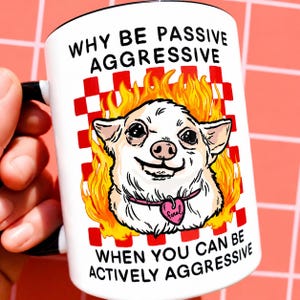 May include: White ceramic mug with a black handle and rim. The mug features a cartoon chihuahua with flames, a pink heart-shaped tag, and the text "WHY BE PASSIVE AGGRESSIVE WHEN YOU CAN BE ACTIVELY AGGRESSIVE."