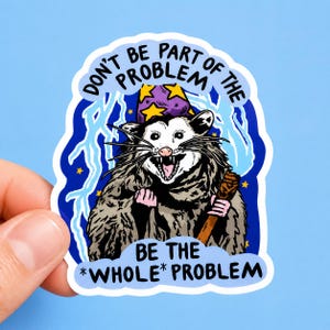 May include: A die-cut sticker featuring a gray opossum wearing a purple wizard hat with yellow stars. The opossum holds a wooden staff against a dark blue background with light blue lightning bolts. Text reads: DON'T BE PART OF THE PROBLEM BE THE *WHOLE* PROBLEM.