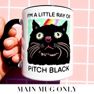 May include: White ceramic mug with a black handle and rim. The mug features a black cat illustration with the text "I'M A LITTLE RAY OF PITCH BLACK". A rainbow and stars are above the cat's head. The mug is held by a hand.