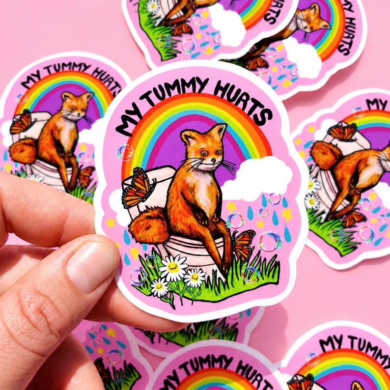 May include: A die-cut sticker featuring a fox sitting on a toilet with the text MY TUMMY HURTS. The design includes a colorful rainbow, monarch butterflies, white daisies, green grass, blue raindrops, and holographic bubbles on a pink background.